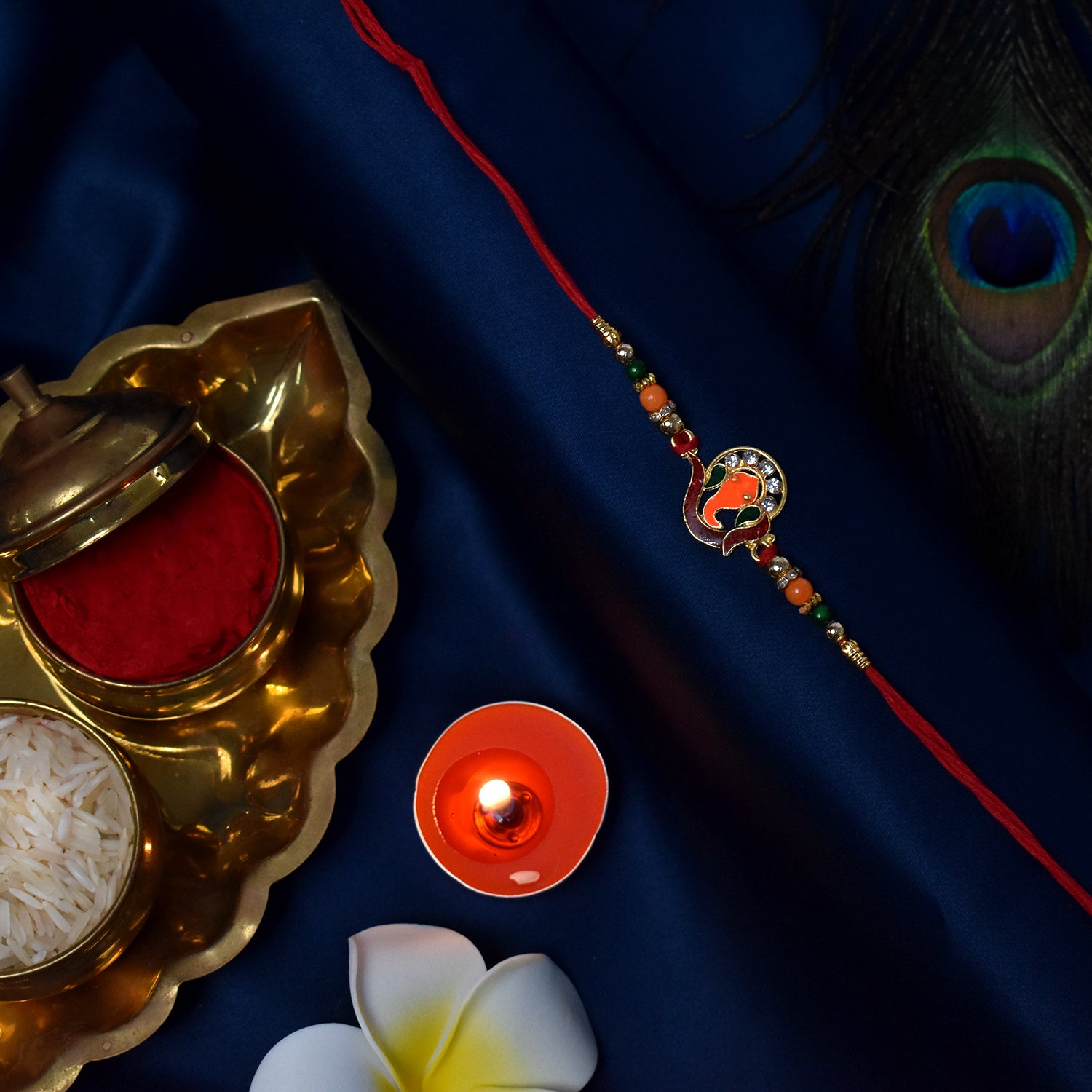 Golden Ganesha Rakhi With Red-green Beads And Stone Detailing Golden Ganesha Rakhi With Red-green Beads And Stone Detailing